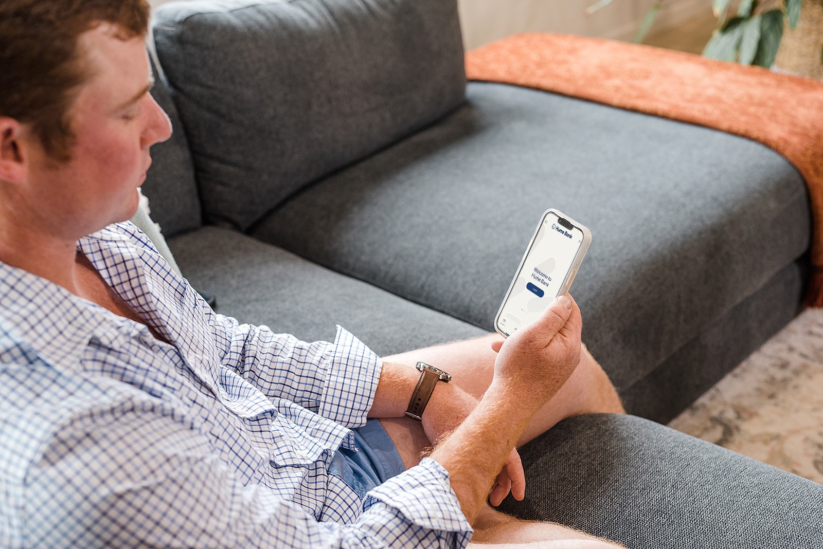 Man sitting on grey couch looking at Hume Bank App on his iPhone.